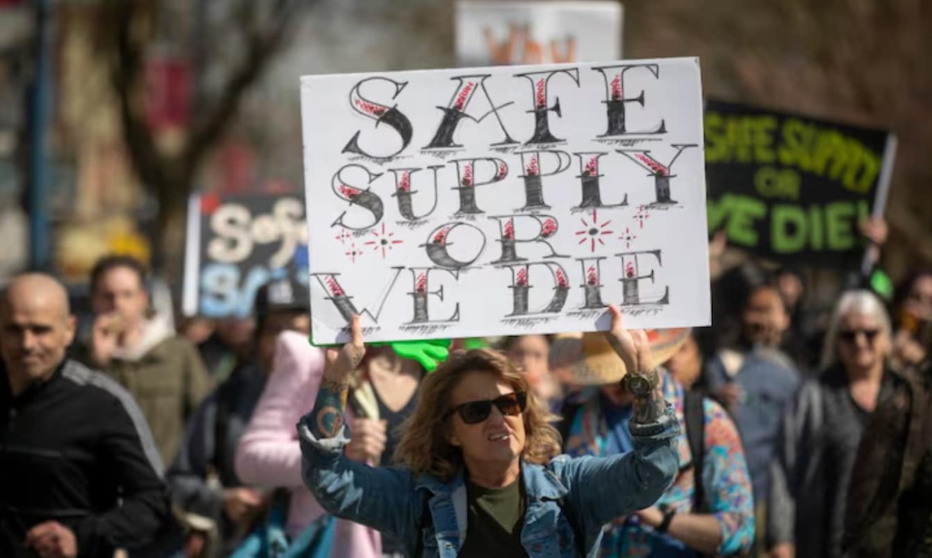 woman holding sign reading "Safe Supply or We Die"